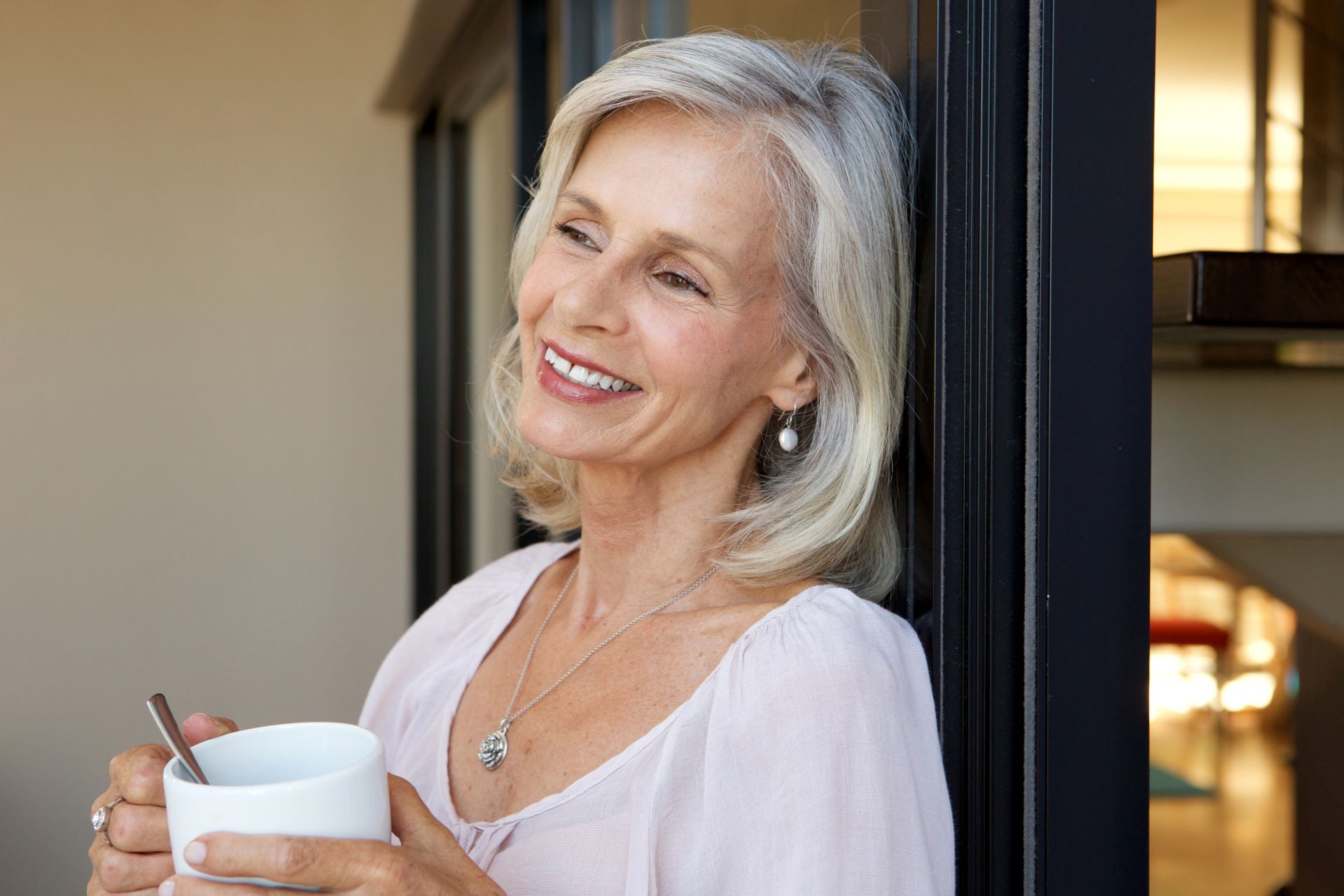 Usmiata žena okolo 55 rokov v období menopauzy odpočíva doma pri okne