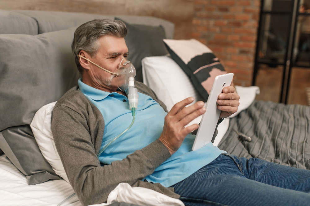 muž inhaluje kyslík cez masku a používa tablet